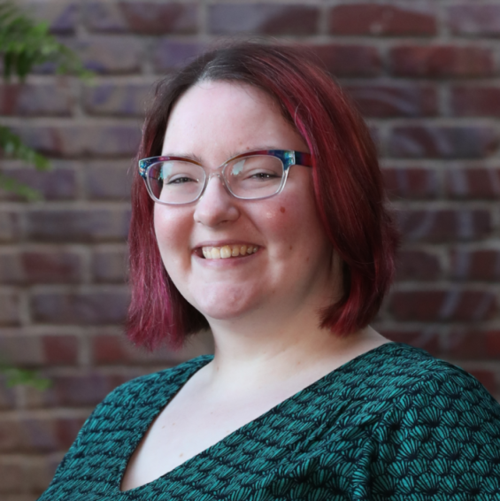 The author, Shimy Moesel, a white person with brown and pink hair and rainbow watercolor glasses, smiling at the viewer.